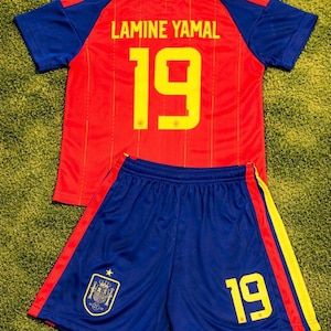 May include: A red and blue soccer jersey and shorts set. The jersey has the name "LAMINE YAMAL" and the number "19" in yellow. The shorts are blue with the number "19" in yellow. The set has the word "España" on the jersey.