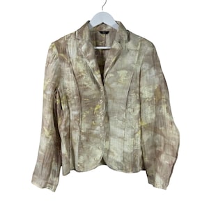 May include: A tan blazer with a subtle pattern, button closure, and long sleeves. The blazer is hanging on a white hanger against a white background. The fabric has a textured appearance with hints of yellow and brown.