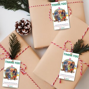 Puede incluir: Cuatro regalos envueltos en papel beige, atados con hilo rojo y blanco y decorados con ramitas verdes. Cada regalo tiene una etiqueta de "Gracias" con una ilustraci&oacute;n de dibujos animados y texto. Tambi&eacute;n se ve una pi&ntilde;a y un cono de hilo.