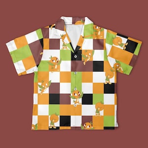 May include: A short-sleeved shirt with a button-down front, showcasing a checkerboard design in orange, brown, green, white, and black. The shirt is decorated with cartoon orange characters.