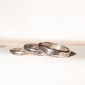 May include: Three silver rings with a textured finish are displayed. One ring has the word "SALTY" engraved, and another has "TY DAV". The rings are set against a light background.