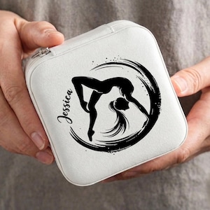 Puede incluir: Una caja de joyería blanca con una silueta negra de una gimnasta en flexión hacia atrás, rodeada por un diseño de pincelada. El nombre "Jessica" está escrito en cursiva. La caja se sostiene en las manos.