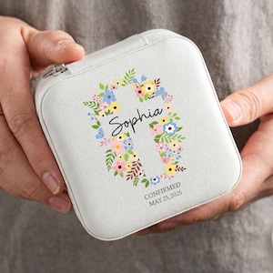 May include: A white, square jewellery case featuring a floral cross design. The name "Sophia" is written in script, surrounded by colourful flowers. The text "CONFIRMED MAY 25, 2025" is also visible.