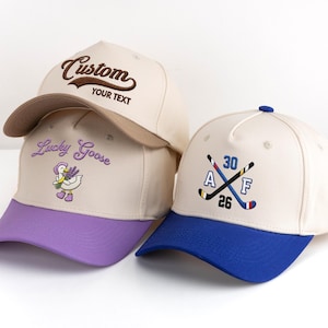 May include: Three baseball caps in cream, with different coloured brims. One cap has "Custom" embroidered on the front, another has "Lucky Goose" with a goose graphic, and the third has crossed hockey sticks and numbers.