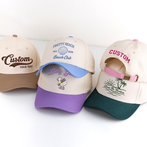 May include: Three baseball caps in cream, brown, blue, and purple. One cap has "Custom" and "YOUR TEXT" embroidered. Another says "PRETTY BEACH" and "Beach Club". The third has "CUSTOM" and "Loves On Vacation" embroidered.
