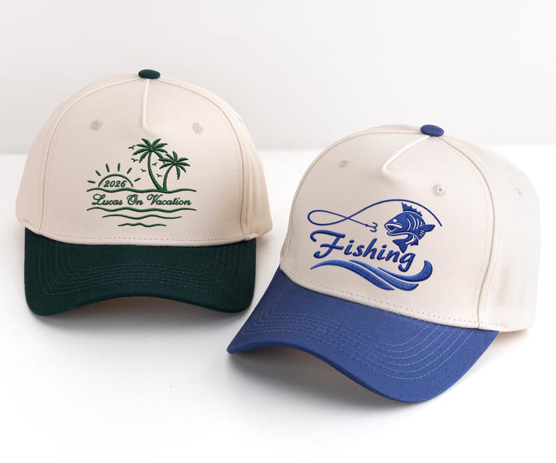 May include: Two baseball caps with contrasting brims. One is cream-coloured with a dark green brim and a palm tree design with the text "2026 Lucas On Vacation". The other is cream-coloured with a blue brim and the word "Fishing" with a fish graphic.