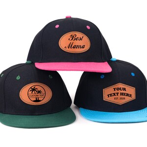 Può includere: Tre cappellini da baseball neri con visiere dai colori contrastanti. Uno ha una visiera rosa e la scritta "Best Mama", un altro ha una visiera verde con un disegno di palme e la scritta "Custom Text", e il terzo ha una visiera blu con la scritta "Your Text Here".