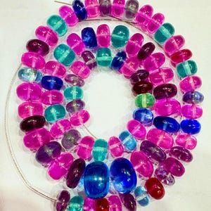 May include: A necklace composed of colorful, translucent beads in shades of pink, blue, green, and purple. The beads are strung on a thin, silver-colored wire, creating a layered design. The beads have an oval shape.