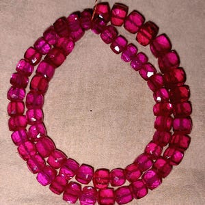 Può includere: Una collana di perline sfaccettate a forma di botte, nei toni del rosa e del magenta. Le perline sono infilate insieme, formando un doppio filo. Le perline sono traslucide e la luce cattura le loro molte sfaccettature.