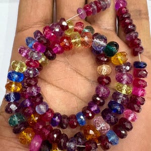 May include: Strands of faceted gemstones in a variety of colors, including red, pink, purple, yellow, and blue. The beads are strung together on a thin, silver-colored wire. The gemstones are of varying sizes and shapes.