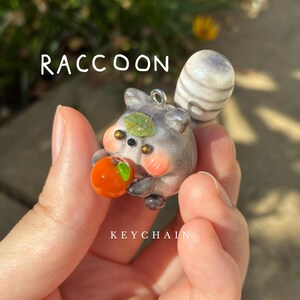 raccoon - handmade polymer clay charm, cute fluffy animal holding fruit keychain, chubby grey raccoon, original clay sculpture whimsy