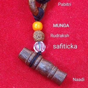 Könnte beinhalten: Nahaufnahme einer Halskette mit schwarzem Kordel und Holz- und Perlenakzenten. Die Halskette hat einen Holzverschluss, eine orangefarbene Perle, eine braune Perle und eine klare, facettierte Perle. Der Text "Pabitri", "MUNGA", "Rudraksh", "safiticka" und "Naadi" ist sichtbar.