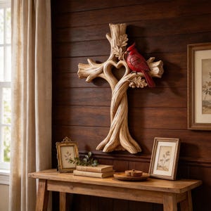 Puede incluir: Una escultura de pared en forma de cruz diseñada para parecer ramas de árbol entrelazadas con un recorte central en forma de corazón. Un pájaro cardenal rojo brillante está posado en el lado derecho de la cruz, que presenta hojas de roble talladas y detalles de corteza texturizada en todo el diseño.