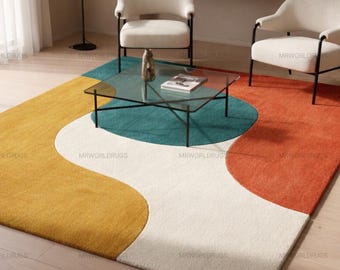 May include: A modern area rug with a colorful, abstract design. The rug features a mustard yellow, teal, white, and orange pattern. A glass coffee table and two white armchairs with black legs are in the background.