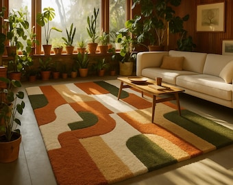 May include: A colorful area rug with an abstract design in shades of orange, green, cream, and tan. The rug is placed in a living room with a sofa, coffee table, and plants. The rug's design features curved and rectangular shapes.