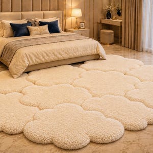 May include: A cream-colored, cloud-shaped rug is laid out on a polished floor in front of a bed. The rug is made of a soft, textured material. The bedroom has a neutral color scheme with beige and cream tones.
