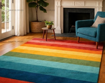 May include: A colorful, striped area rug with a rainbow of colors, including red, orange, yellow, green, and blue. The rug is rectangular and placed on a hardwood floor. The room also features a blue armchair, a fireplace, and a large plant.