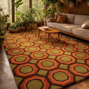 May include: A patterned rug featuring a repeating design of orange and olive green hexagons. The rug is in a room with a neutral sofa, wooden coffee table, and numerous potted plants. The room has a retro aesthetic, with a warm, inviting atmosphere.
