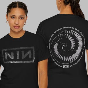 May include: Black t-shirts with Nine Inch Nails band designs. One shirt shows "NIN" in a rectangle. The other has a spiral design with text, including "NIN". Both shirts are worn by a person. The text is in white.