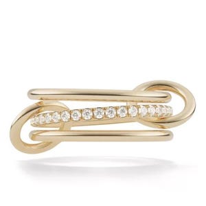 Peut inclure: Une bague dorée au design unique et lié. La bague présente une rangée de petits pierres précieuses transparentes. Le design comprend plusieurs boucles imbriquées, créant un look moderne et élégant. Un bijou élégant.