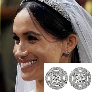 May include: A close-up of a woman wearing a diamond tiara and veil. The image also shows a pair of round, silver earrings with a central diamond surrounded by smaller stones. The earrings have a geometric design.