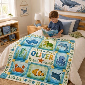 May include: A rectangular quilt featuring a grid of illustrations of sea creatures including a whale, turtle, dolphin, seahorse, octopus, crab, clownfish, and stingray. The center panel displays the name OLIVER in large, colorful letters.