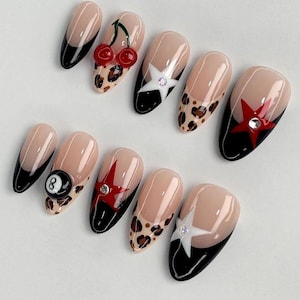 May include: A set of ten artificial nails with various designs. The nails feature a nude base with black tips, leopard print, cherries, stars, and an 8-ball. Some nails have rhinestones for added sparkle.