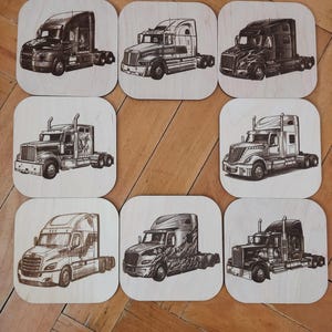 May include: Nine square wooden coasters with engraved illustrations of articulated lorries. Each coaster features a different lorry design, showcasing various styles and details. The coasters are arranged on a wooden surface.