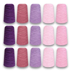 May include: A collection of fifteen yarn cones in shades of purple, pink, and red. The cones are arranged in three rows of five, showcasing a variety of colors suitable for knitting and crochet projects. The yarn is tightly wound.