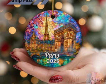 May include: A circular Christmas ornament with a stained-glass effect, showcasing Parisian landmarks like the Eiffel Tower and Arc de Triomphe. The ornament displays the text "Paris 2025" and is hung by a gold string.