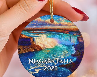 May include: Round Christmas ornament featuring a vibrant depiction of Niagara Falls. The ornament has a gold string for hanging and includes the text "Niagara Falls 2025". The background shows a colorful sky and the cascading water of the falls.