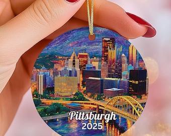 May include: A round Christmas ornament featuring a colorful cityscape of Pittsburgh, Pennsylvania, with the text "Pittsburgh 2025". The ornament has a gold string for hanging.