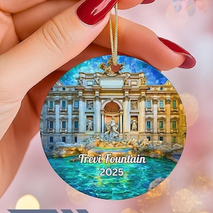 May include: Circular Christmas ornament depicting the Trevi Fountain in Rome, Italy, with the text "Trevi Fountain 2025". The ornament has a gold hanging string and is held by a hand. The ornament has a blue and gold mosaic design.