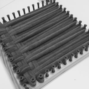 Puede incluir: Primer plano de un telar con hilo negro tejido en un patr&oacute;n cuadrado. El telar est&aacute; hecho de madera y tiene clavijas negras alrededor de los bordes.