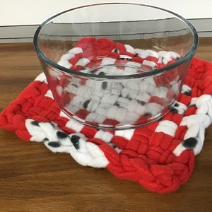 May include: A red and white woven pot holder with black polka dots. A clear glass bowl sits on top of the pot holder.