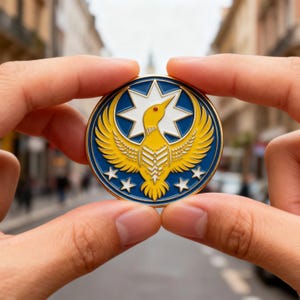 May include: A round, blue and gold coin featuring a stylized yellow bird with outstretched wings, a white star, and five smaller stars. The coin is held between two hands against a blurred street background.