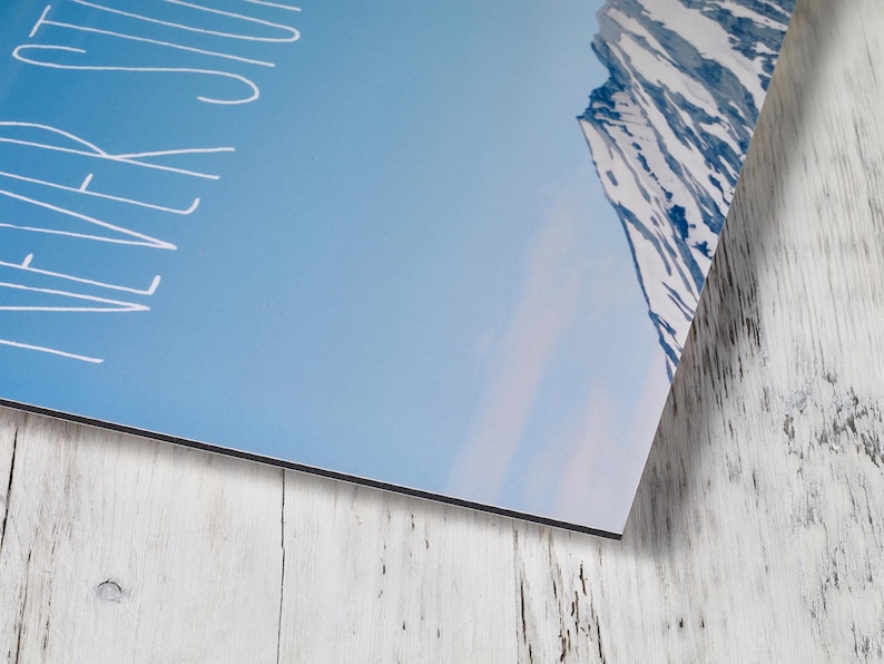 May include: A rectangular wall art print featuring a blue sky and a snow-covered mountain peak on the right side. The white text "NEVER STOP" is printed vertically along the left edge of the image in a simple, clean, hand-drawn style font.
