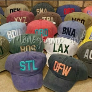 May include: A collection of 18 different colored baseball caps with various city airport codes embroidered on the front. The caps are made of a soft, cotton fabric and have a classic, vintage look.