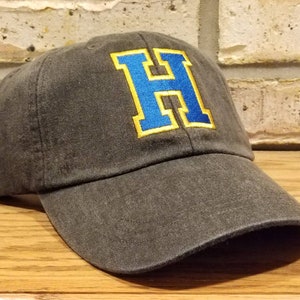 May include: A black baseball cap with a large blue and yellow embroidered letter "H" on the front.