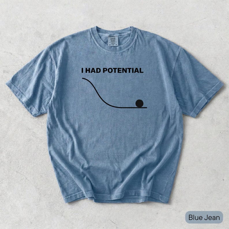 Pode incluir: Uma t-shirt de manga curta na cor azul jeans com o texto preto I HAD POTENTIAL acima de um gr&aacute;fico preto de uma linha curva que desce para uma superf&iacute;cie plana com um pequeno c&iacute;rculo preto no final da linha no lado direito.