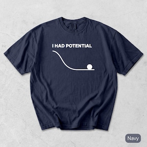 Pode incluir: Uma t-shirt azul-marinho de manga curta com um gr&aacute;fico branco que mostra um diagrama de f&iacute;sica com uma linha curva e um c&iacute;rculo sobre uma superf&iacute;cie plana. Acima do gr&aacute;fico, o texto I HAD POTENTIAL aparece em letras mai&uacute;sculas brancas.