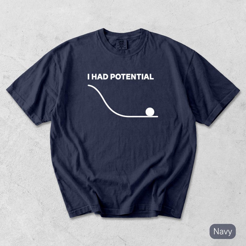 Pode incluir: Uma t-shirt azul-marinho de manga curta com um gr&aacute;fico branco que mostra um diagrama de f&iacute;sica com uma linha curva e um c&iacute;rculo sobre uma superf&iacute;cie plana. Acima do gr&aacute;fico, o texto I HAD POTENTIAL aparece em letras mai&uacute;sculas brancas.
