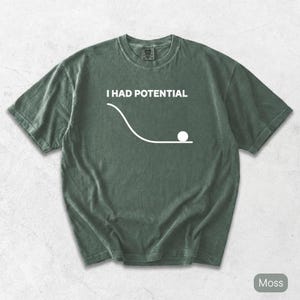 Pode incluir: Uma t-shirt de manga curta verde musgo com um gr&aacute;fico branco de uma curva descendente que termina numa linha plana com um c&iacute;rculo, acompanhada pelo texto branco "I HAD POTENTIAL" impresso numa fonte sem serifa na zona do peito.