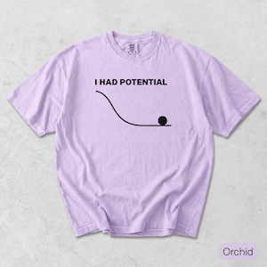 Pode incluir: Uma t-shirt de manga curta em violeta claro com o texto preto I HAD POTENTIAL sobre um gr&aacute;fico de uma linha curva e um c&iacute;rculo preto s&oacute;lido que representa uma bola no fundo de uma inclina&ccedil;&atilde;o. A t-shirt tem gola redonda e corte padr&atilde;o.