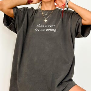 Op de afbeelding: Donkergrijs t-shirt met de witte tekst "miss never do no wrong". Het shirt heeft korte mouwen en een relaxte pasvorm. Het is een casual kledingstuk.