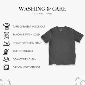 May include: A charcoal gray t-shirt with short sleeves, displayed on a white background. The image includes washing and care instructions: turn garment inside out, machine wash cold, do not iron on print, do not bleach, do not dry clean, and dry on low settings.