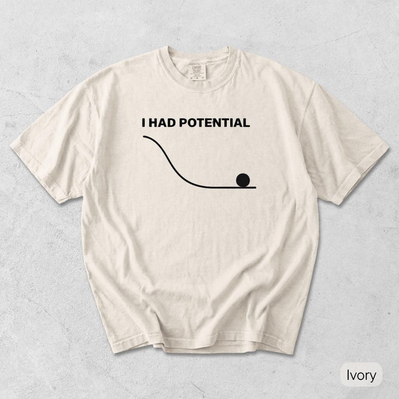 Pode incluir: Uma t-shirt de manga curta na cor marfim com um gr&aacute;fico preto de uma linha curva que leva a uma superf&iacute;cie plana com um c&iacute;rculo preto s&oacute;lido no final. Acima do gr&aacute;fico, o texto I HAD POTENTIAL est&aacute; escrito numa fonte preta, negrito e sem serifa.