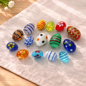 May include: A selection of decorative glass egg ornaments in various colours and patterns. Designs include stripes, polka dots, floral, and abstract swirls. The eggs are arranged on a white cloth, showcasing their vibrant hues.