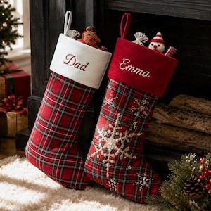 Könnte beinhalten: Zwei Weihnachtsstrümpfe mit Aufhängeschlaufen. Der linke Strumpf hat einen weißen Umschlag mit der Stickerei 'Dad' und ein rot kariertes Muster. Der rechte hat einen roten Umschlag mit 'Emma', rot kariertem Stoff und goldenen Schneeflocken.