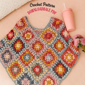 May include: A colorful, crocheted poncho featuring a patchwork design of squares in shades of pink, yellow, blue, and red. The text "Crochet Pattern DOWNLOADABLE PDF" is visible. A pink tumbler and pink flowers are also in the image.